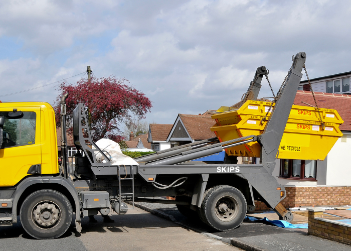 A skip being unloaded from a parked transport lorry.